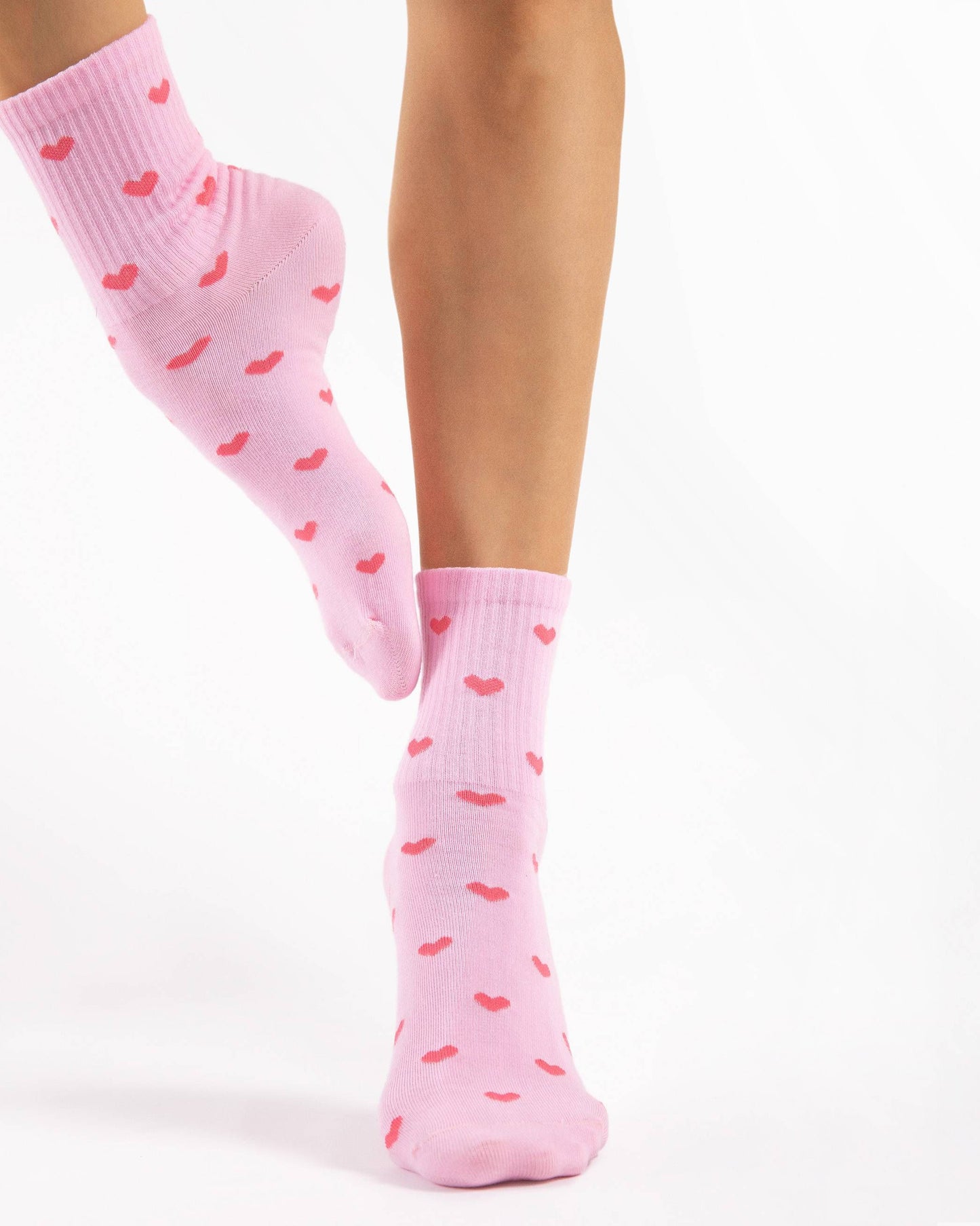 Fiore Loves Sock - Light pink ankle socks with all over pink heart pattern and ribbed cuff. Model balanced on 1 foot.