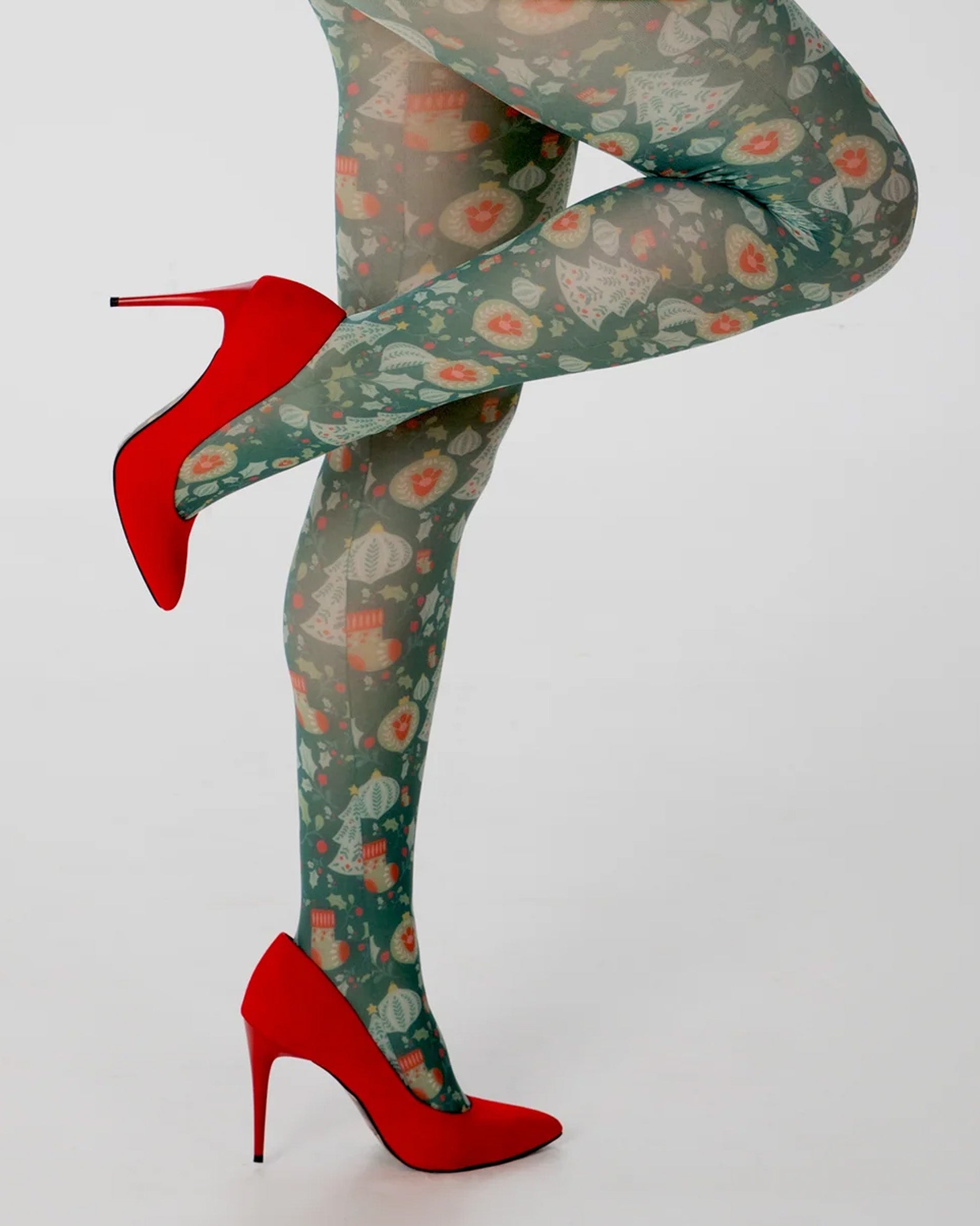 Pamela Mann Christmas Chaos Tights - White opaque tights with a Christmas themed print of Xmas trees, baubles, stockings & holly in shades of green and red. Worn with red stilettos.