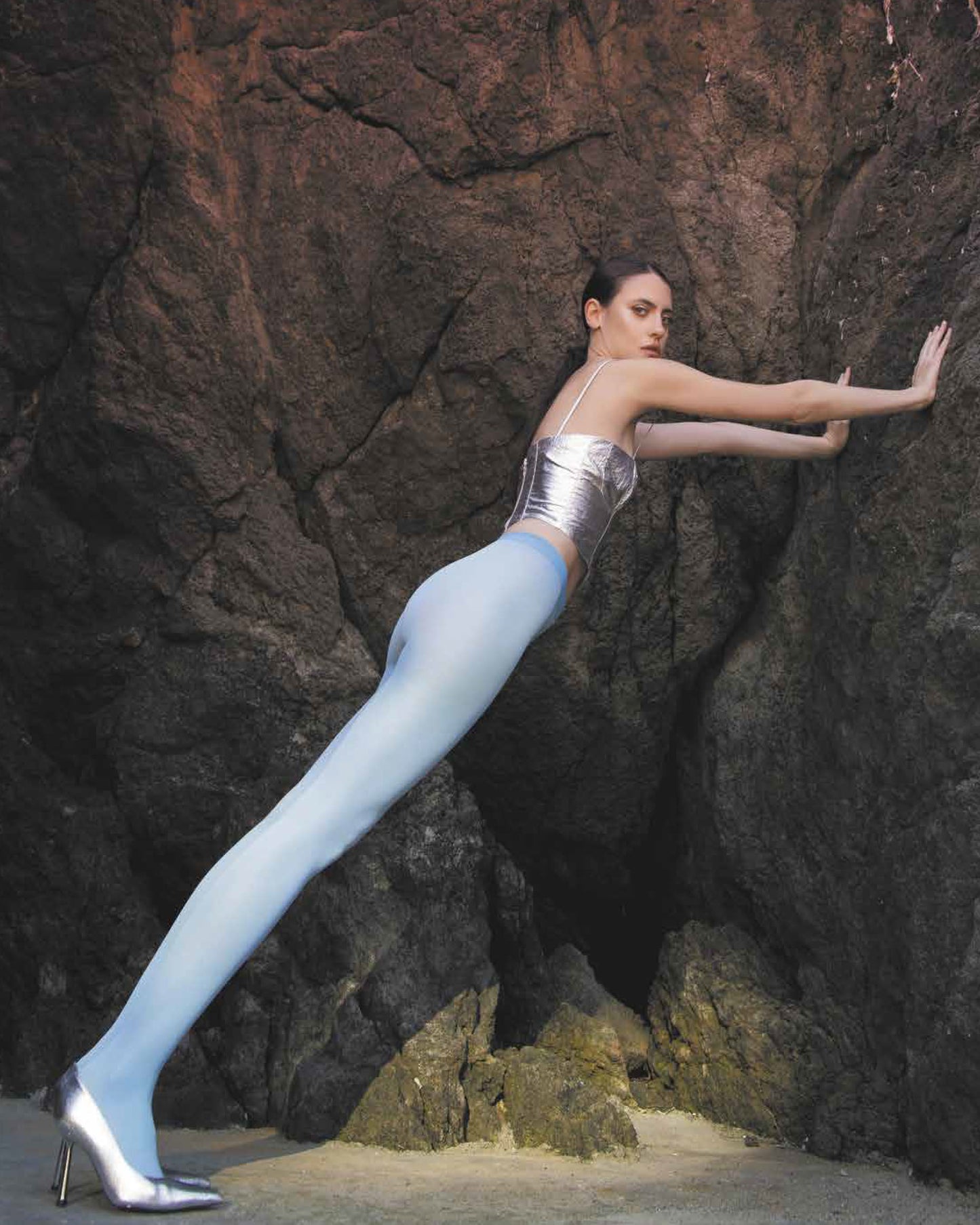 Trasparenze Sophie 70 Collant - coloured opaque tights in light azzurro blue worn by model wearing silver heels leaning on rocky background.