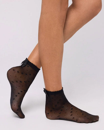 Ysabel Mora 16616 Heart & Bow Socks - Sheer black fashion ankle socks with a diagonal pattern of hearts and spots, scalloped cuff with a satin bow on the back. Side view.