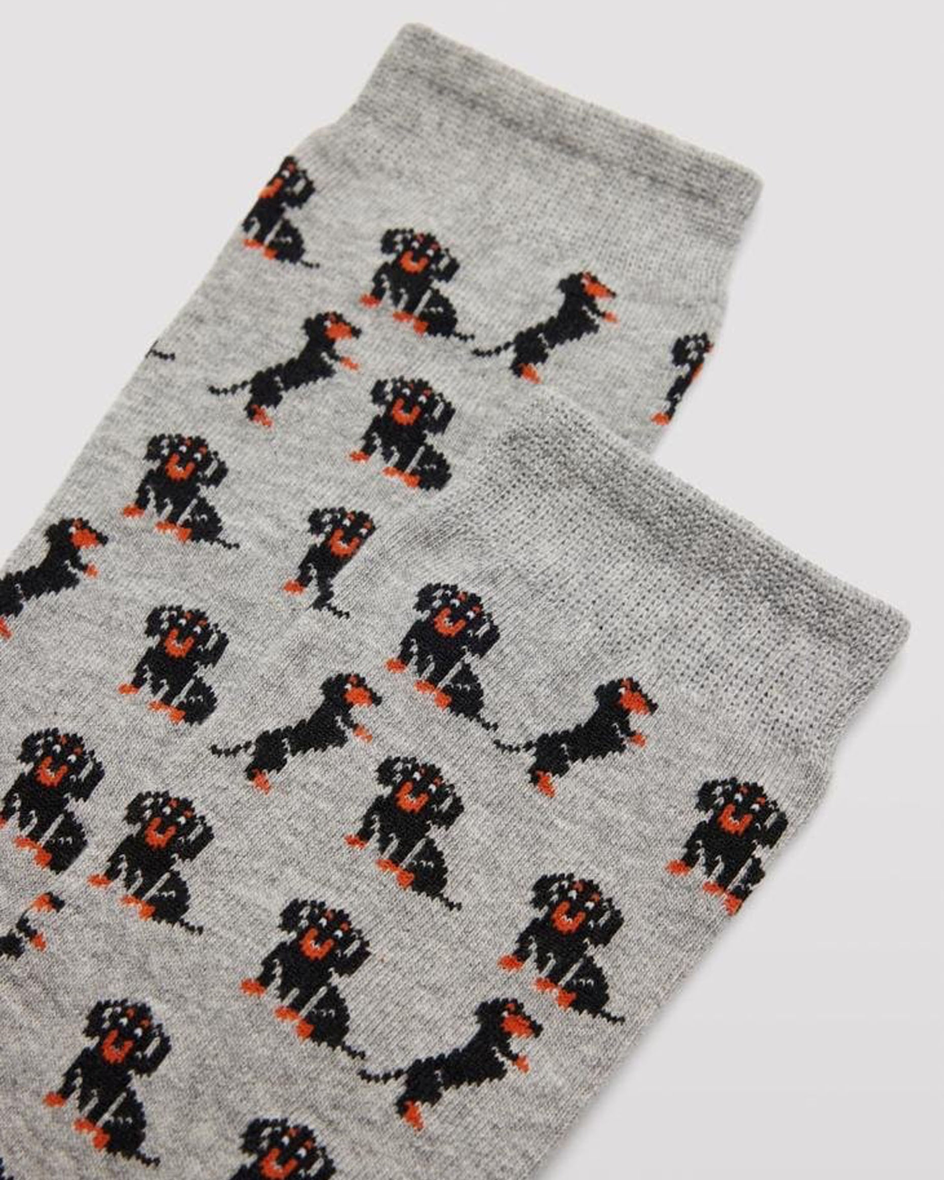 Ysabel Mora Dachshund Sock - Men's light grey cotton crew length ankle socks with an all over pattern of cute black and brown dachshunds (a.k.a sausage dogs) with soft anti-pressure cuffs. Close up detail.