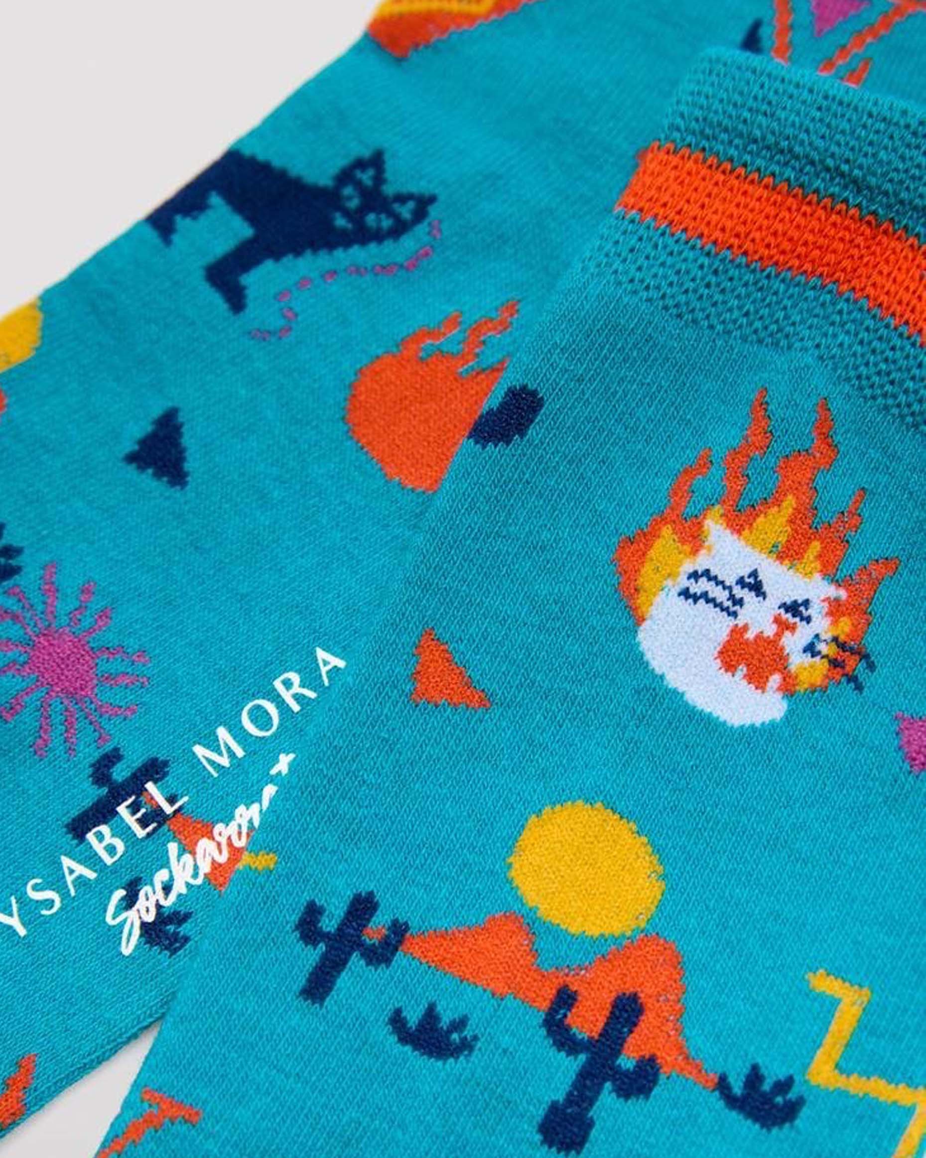 Ysabel Mora 22175 Desert Cats - Turquoise cotton crew length ankle socks with an all over Mexican desert themed pattern of cactus, hills, sun, cats, fire flames and tequila bottles light yellow heel and toe with soft anti-pressure cuffs. Close up detail.