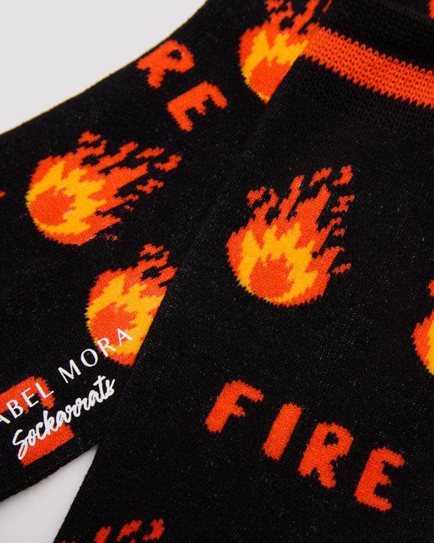 Ysabel Mora 22175 Fire Sock - Men's black cotton crew length ankle socks with an all over pattern of fire and flames in orange and yellow, orange stripe on cuff, orange heel and toe with soft anti-pressure cuffs. Close up detail.