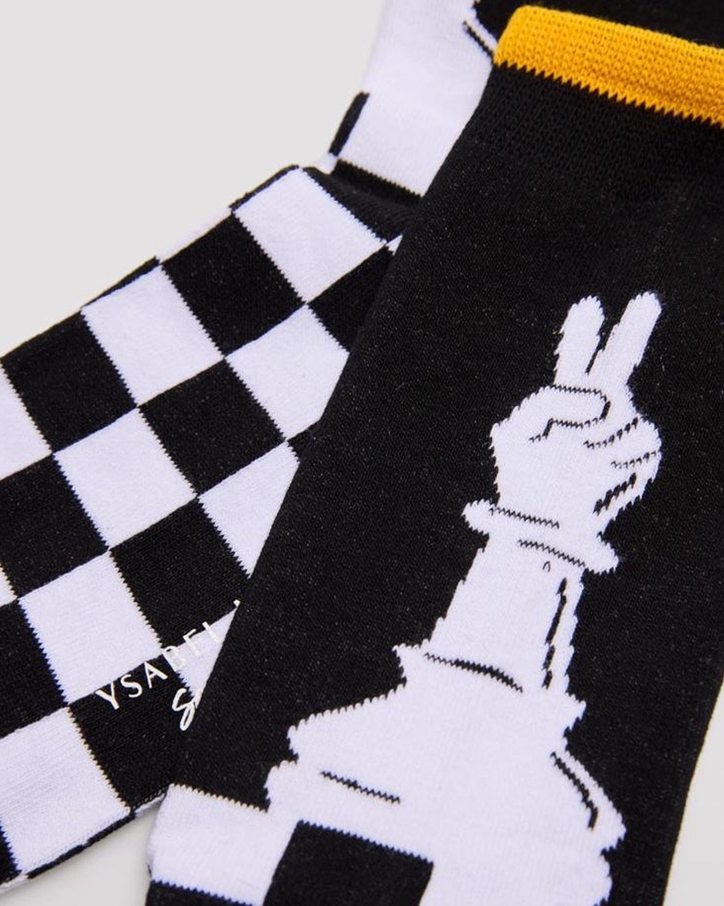 Ysabel Mora 22179 Chess Sock - Men's cotton crew length ankle socks with a chess themed design of a chessboard and pawn piece with a hand on top giving the peace sign and soft anti-pressure cuff with a yellow stripe on edge. Close up detail.