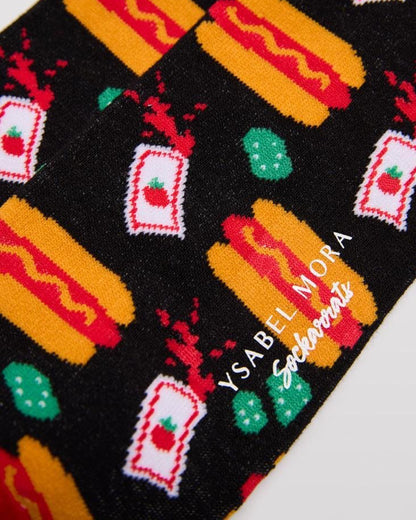 Ysabel Mora 22179 Hot Dog Sock - Men's black cotton crew length ankle socks with an all over pattern of hot dogs with mustard sauce, packets of tomato ketchup and jerkins, red toe and heel and soft anti-pressure cuff with a red stripe on edge. Close up detail.