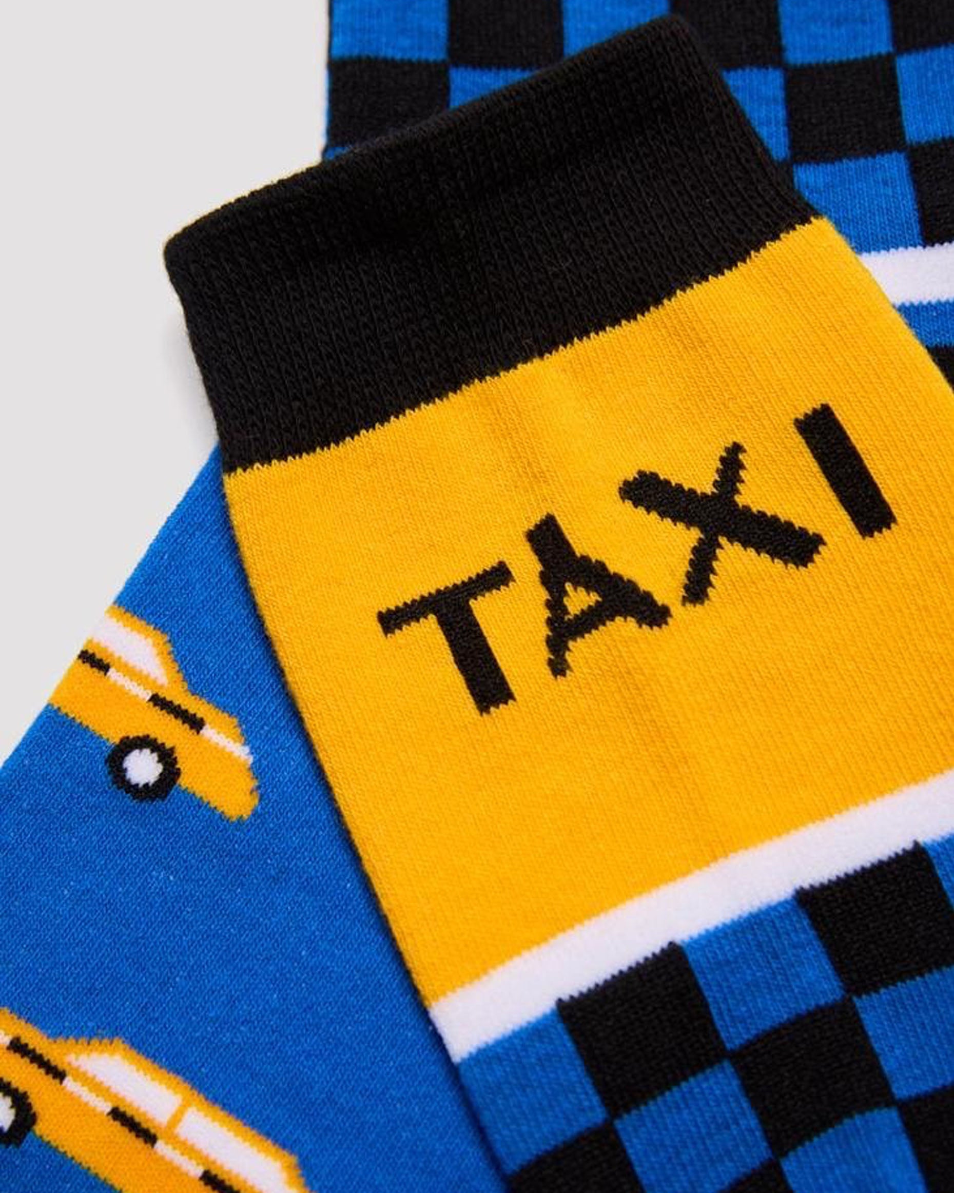 Ysabel Mora 22179 Taxi Sock - Men's cotton crew length ankle socks with an New York cab themed design with taxi written on the cuff in black with yellow background, checkered black and blue pattern underneath and then a pattern of yellow taxis in the foot, black heel and toe and soft black anti-pressure cuffs. Close up detail.