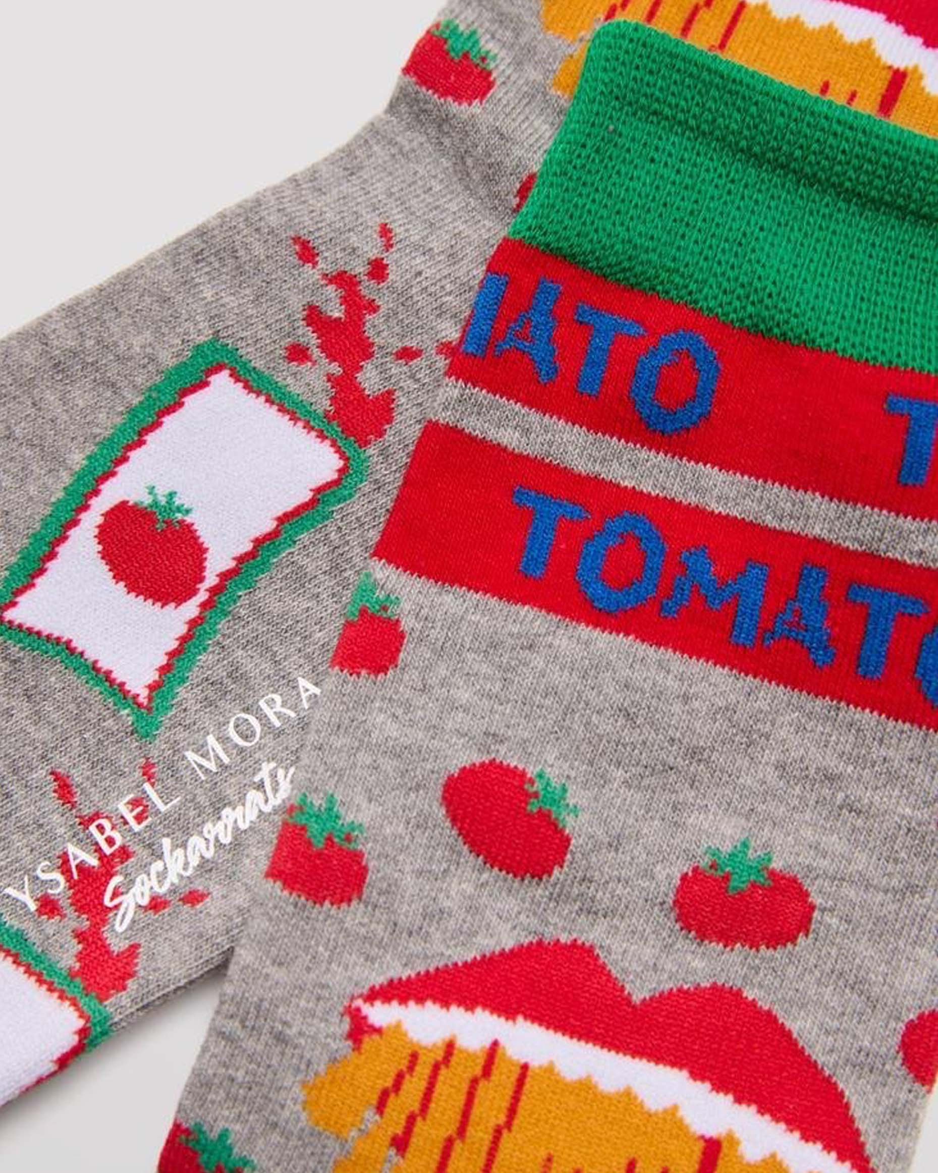 Ysabel Mora Tomato Socks - Men's light grey cotton crew length ankle socks with an all over pattern of tomatoes, sachets of tomato ketchup, tomato written around the cuff green toe and heel and soft anti-pressure cuff. Close up detail.