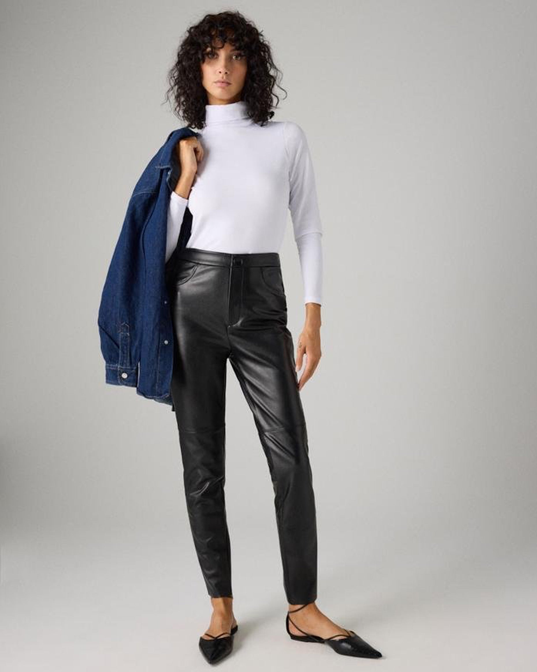 Ysabel Mora 70420 Faux Leather Pants - Black faux leather thermal relaxed fit trouser leggings with fly and button closure, faux front pocket stitching, tapered leg and soft, warm plush fleece lining. Worn with white polo neck.