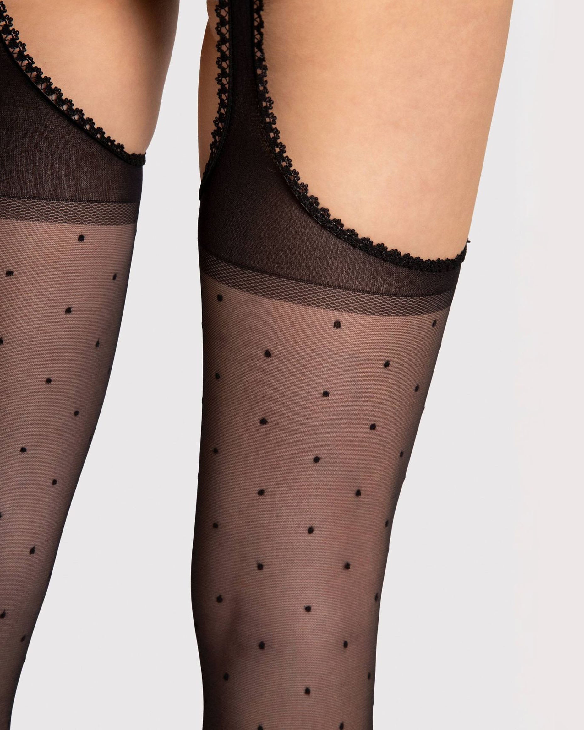 Sheer black suspender tights with a small polka dot spot pattern open sides and crotchless with a scalloped edge. Close up detail.