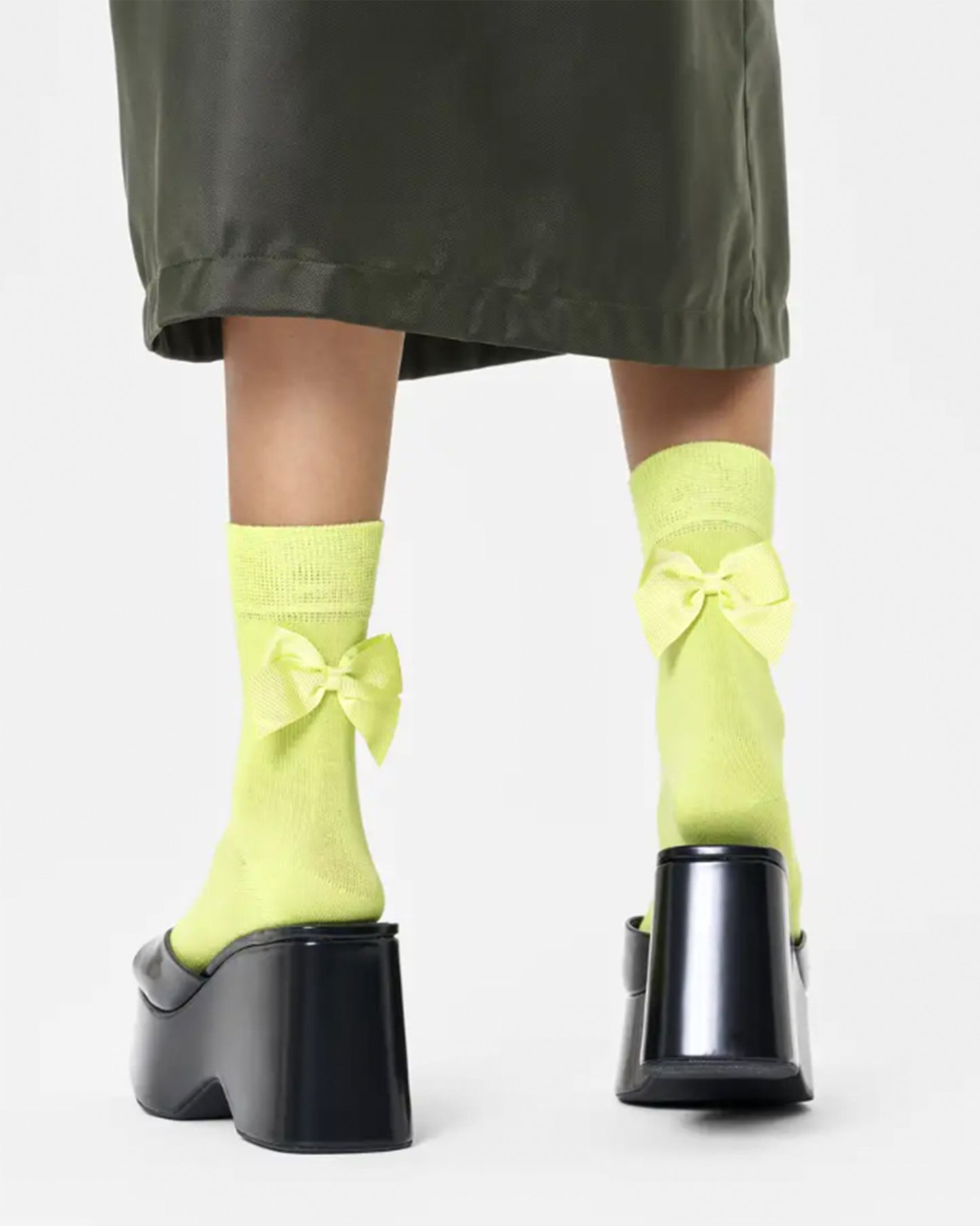 Happy Socks Bow Sock - Bright lime green quarter high (1/2 crew) cotton socks with same colour satin bows on the back, deep cuff, shaped heel and flat toe seam. Back view. Worn with black mules and khaki green skirt.